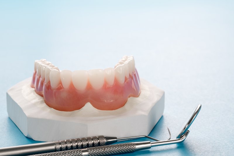 A closeup of a loose lower denture next to a dental tool