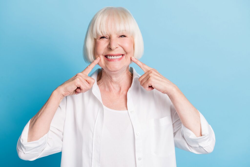 Woman with short white hair pointing to her smile with two fingers