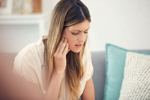 Concerned woman sitting on couch rubbing her jaw